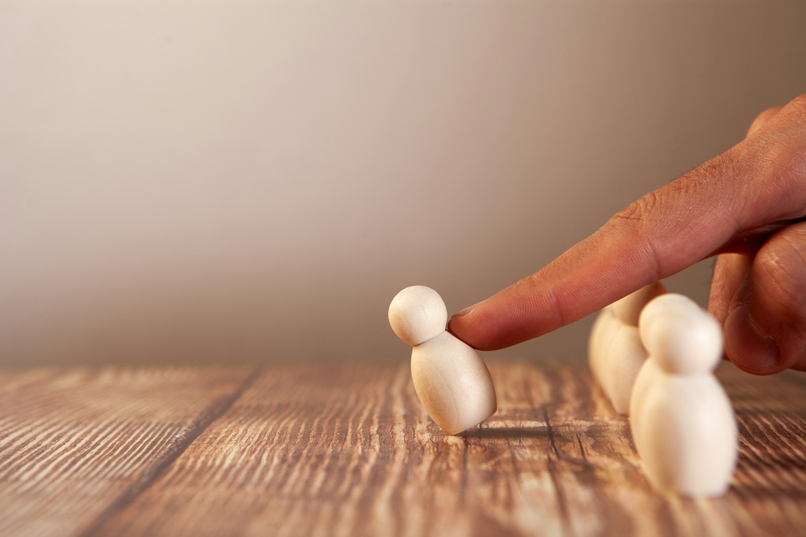 A hand nudging one wooden figure forward from a group